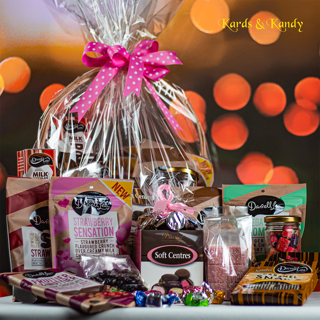 Indulgence chocolate gift basket wrapped in cellophane with a pink bow, surrounded by chocolates and sweets